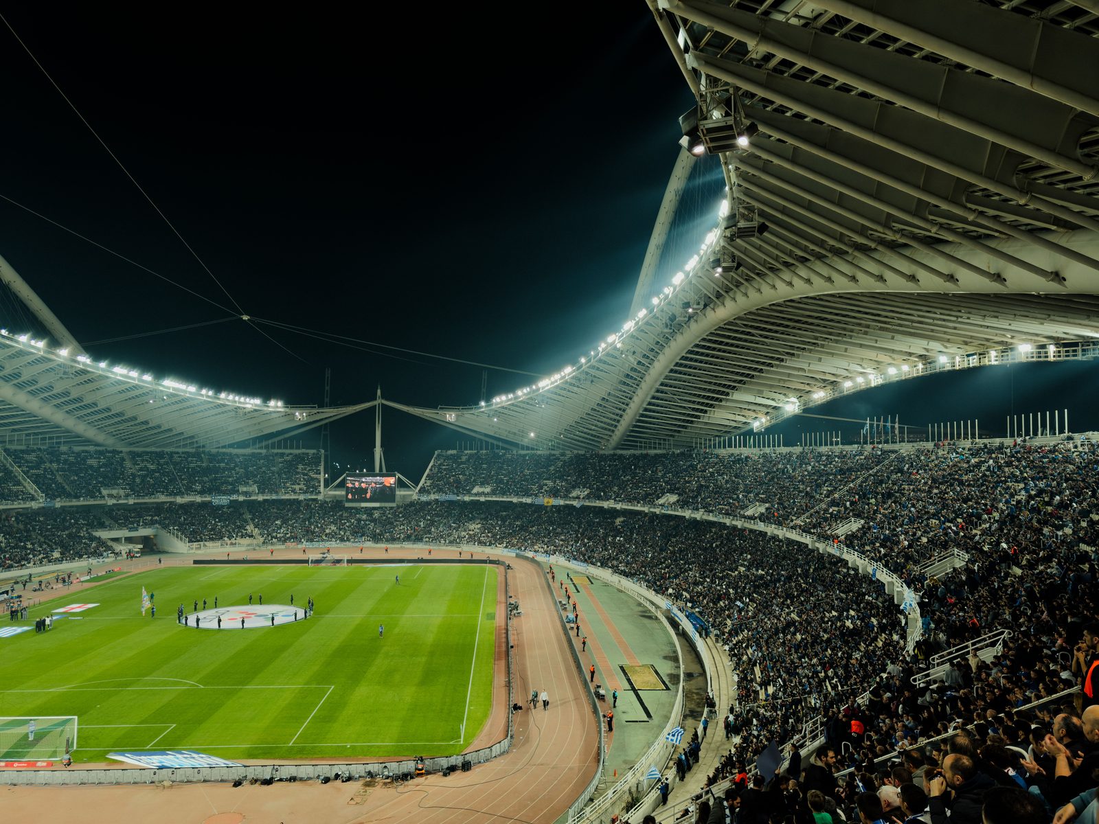 Estadio de fútbol iluminado por la noche durante un partido, con público en las tribunas